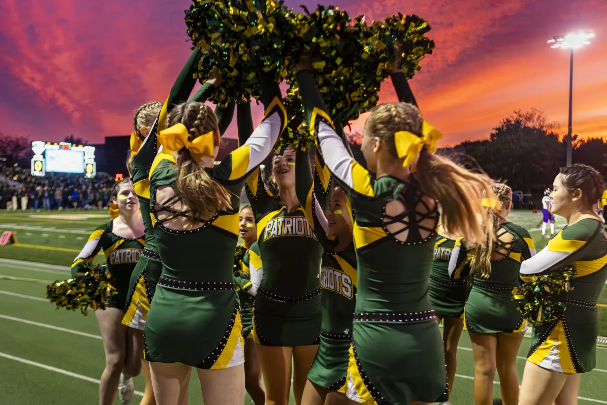 The Girls Varsity Cheerleading team celebrates on the sidelines before the game. In addition to sideline cheer, they also perform during the halftime show.