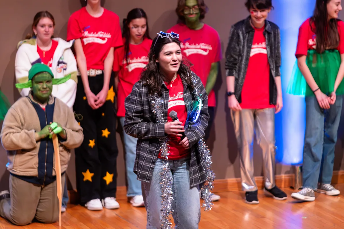 FPC member Rachel Kierzkowski '26 stands at the front of the stage with a microphone during the opening game of the show. Members performed in multiple games throughout the show and rotated.